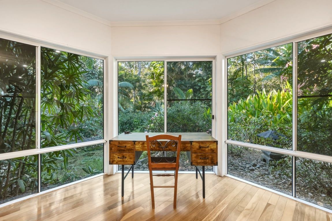 Una stanza con una scrivania e una sedia in legno, ampie finestre e vista su un giardino.
