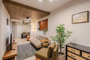 Una sala de estar moderna con sofá, mesa de centro, televisor sobre un mueble, ventilador de techo y planta en maceta.