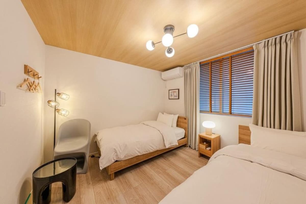 Un dormitorio con dos camas, una mesita de noche, una silla, una lámpara de pie y una lámpara en el techo.