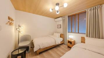 A bedroom with two beds, a bedside table, a chair, a floor lamp, and a ceiling light fixture.