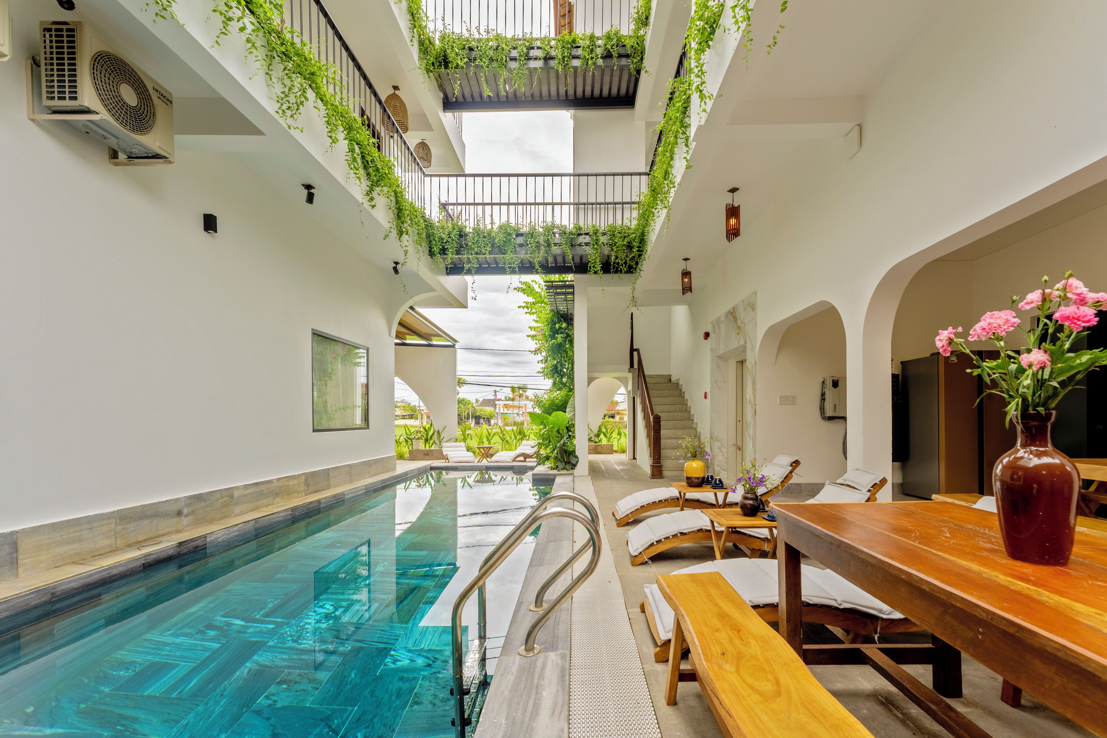 Zona de piscina con vista despejada, sillones de descanso y una mesa de madera con un florero.