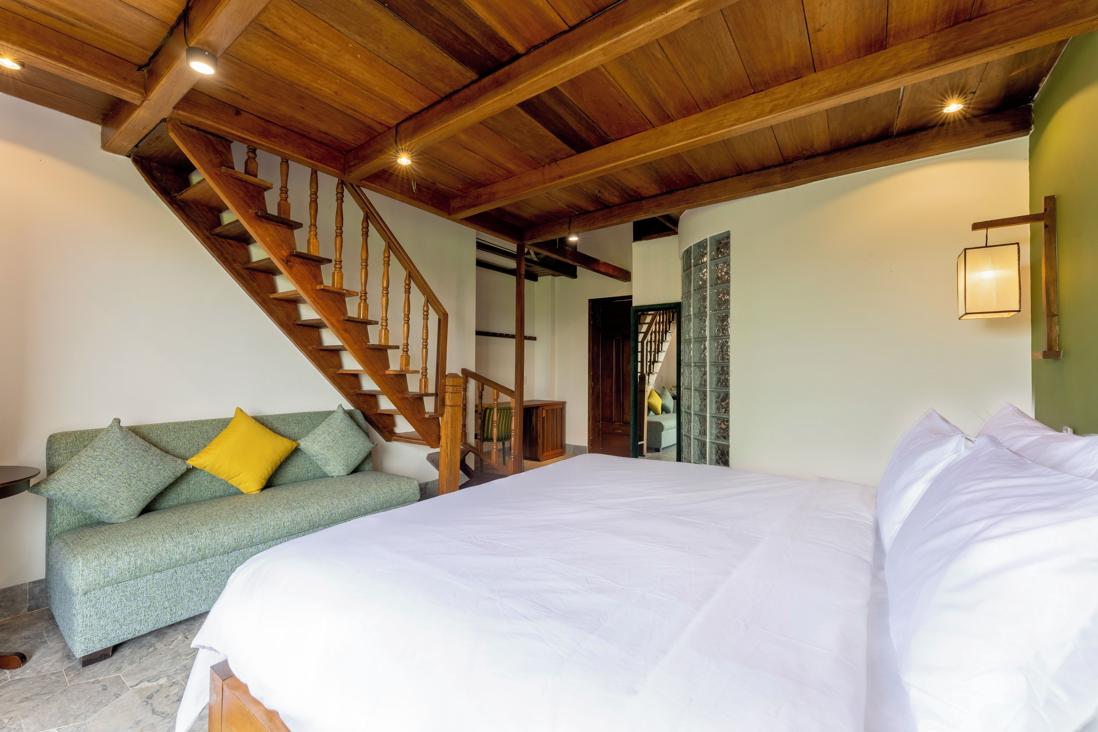 Un dormitorio con una cama grande, una escalera de madera, un sofá verde con cojines amarillos y una pared verde.