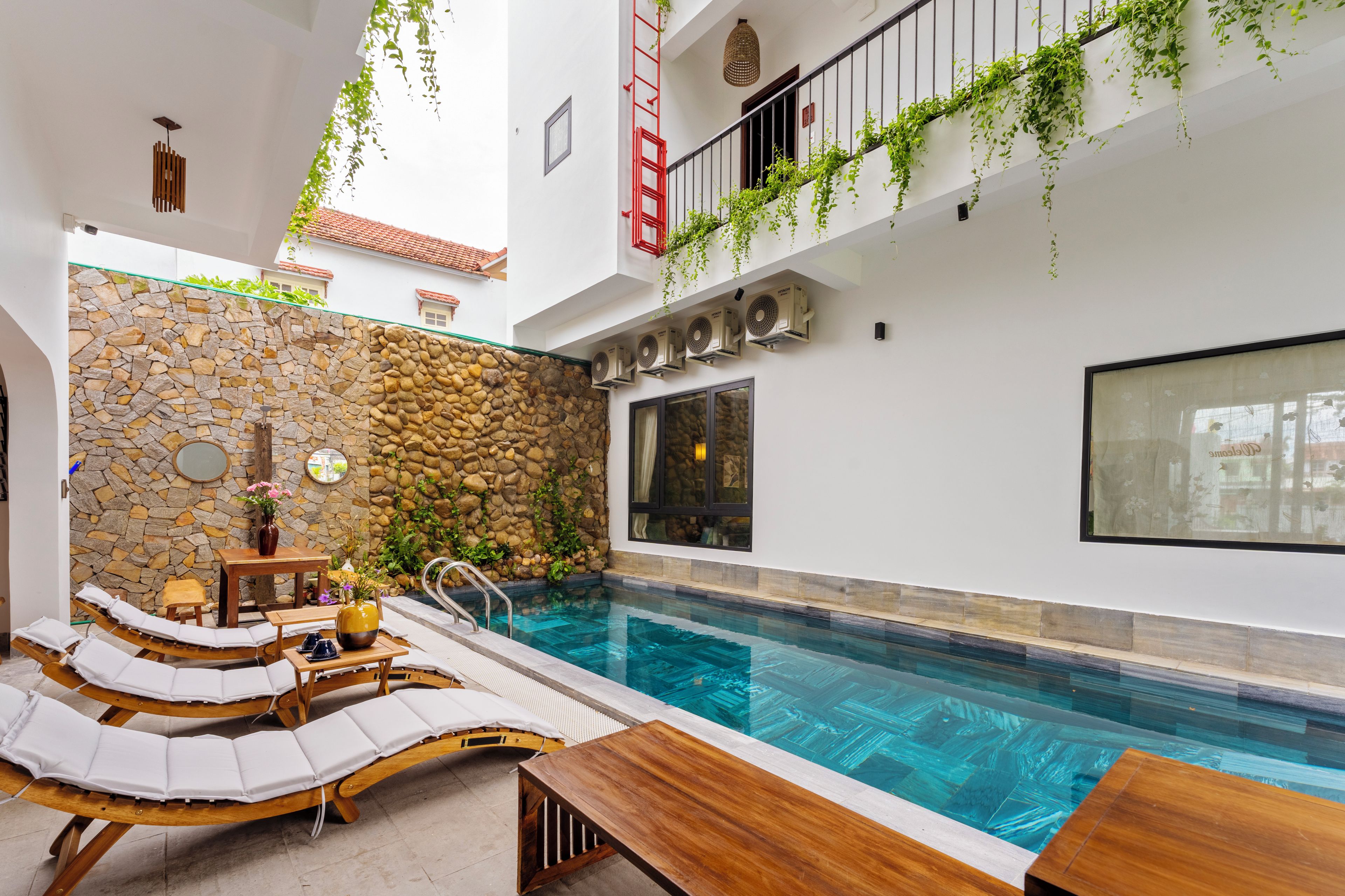 Un área de piscina con sillones de descanso, un muro de piedra y un equipo de aire acondicionado.