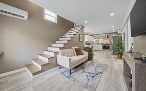 Uma sala de estar moderna com escada, um sofá, uma mesa de centro e uma cozinha ao fundo.