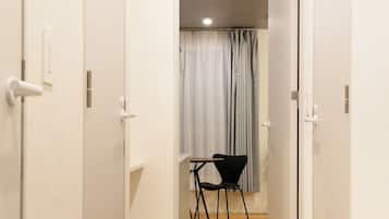 A narrow hallway with wooden flooring leading to a room with a table and chairs.