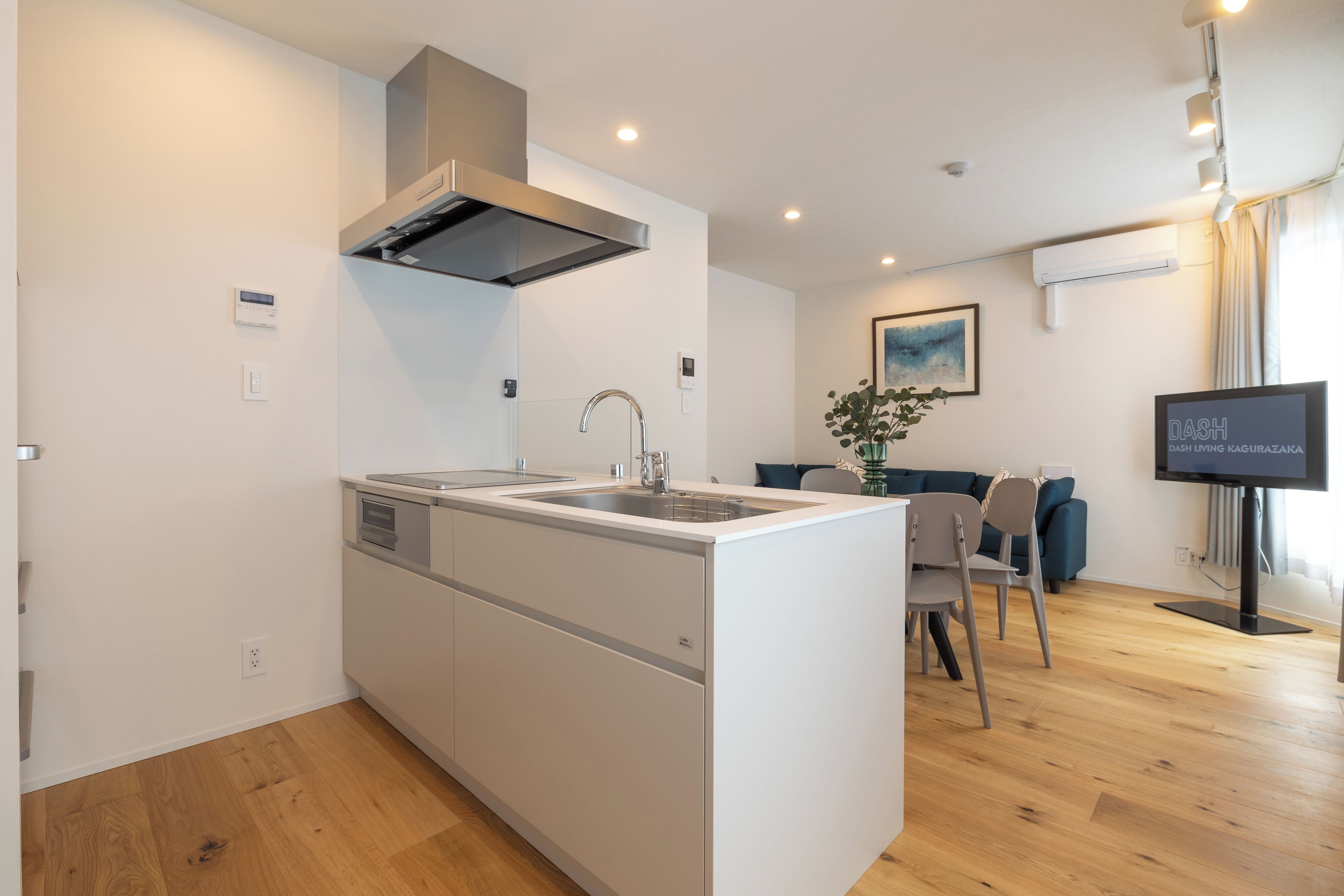 A modern kitchen with a built-in island, a dining area with a table and chairs, and a living room with a sofa and a flat-screen TV.