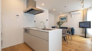 A modern kitchen with a built-in island, a dining area with a table and chairs, and a living room with a sofa and a flat-screen TV.