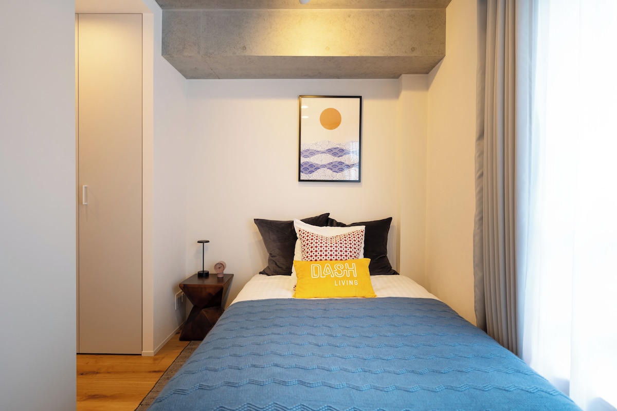 Quarto com cama, travesseiros, mesa de cabeceira, relógio e quadro na parede.