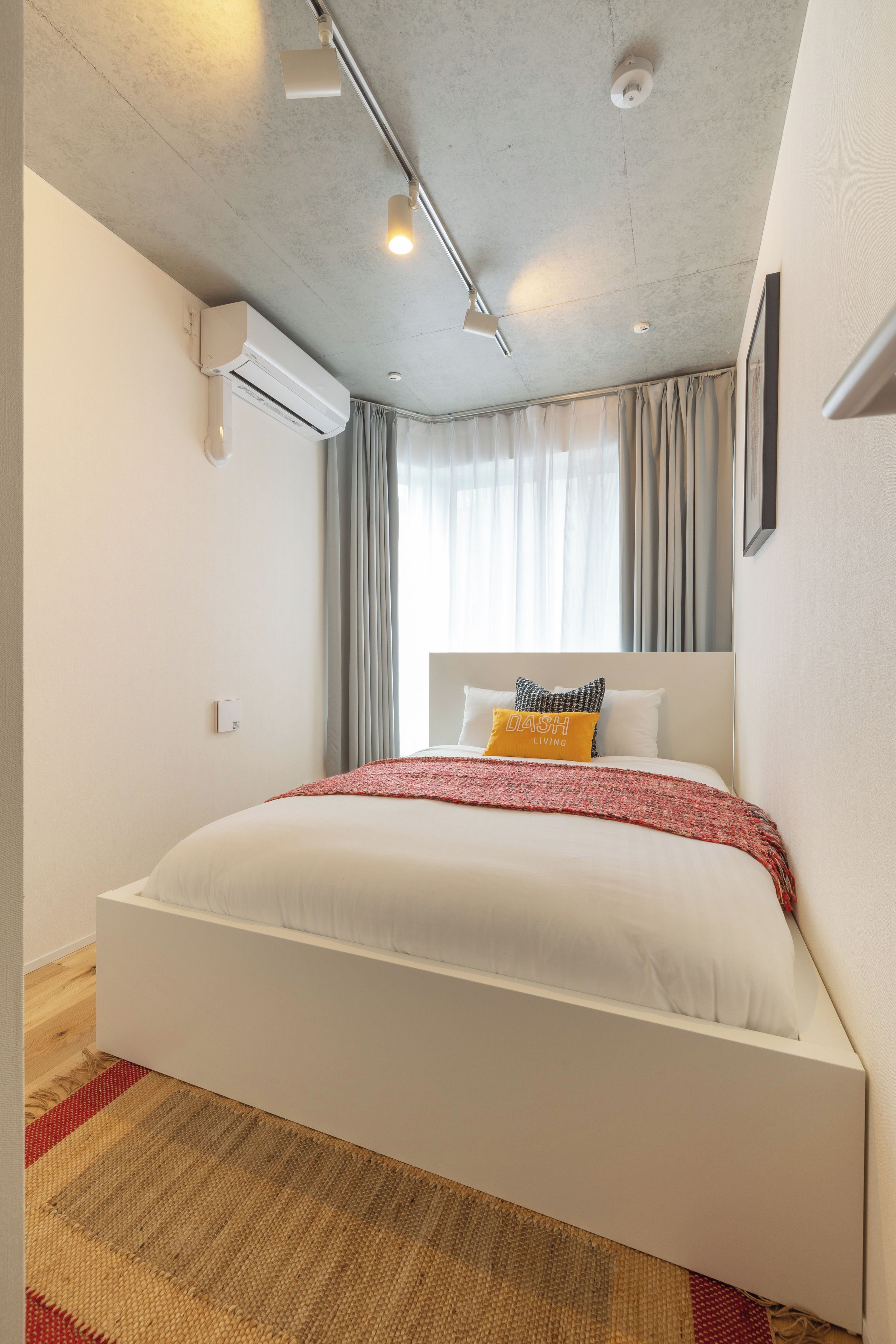 A modern hotel room with a large bed, a ceiling fan, an air conditioning unit, and a window with curtains.
