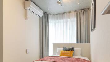 A modern hotel room with a large bed, a ceiling fan, an air conditioning unit, and a window with curtains.