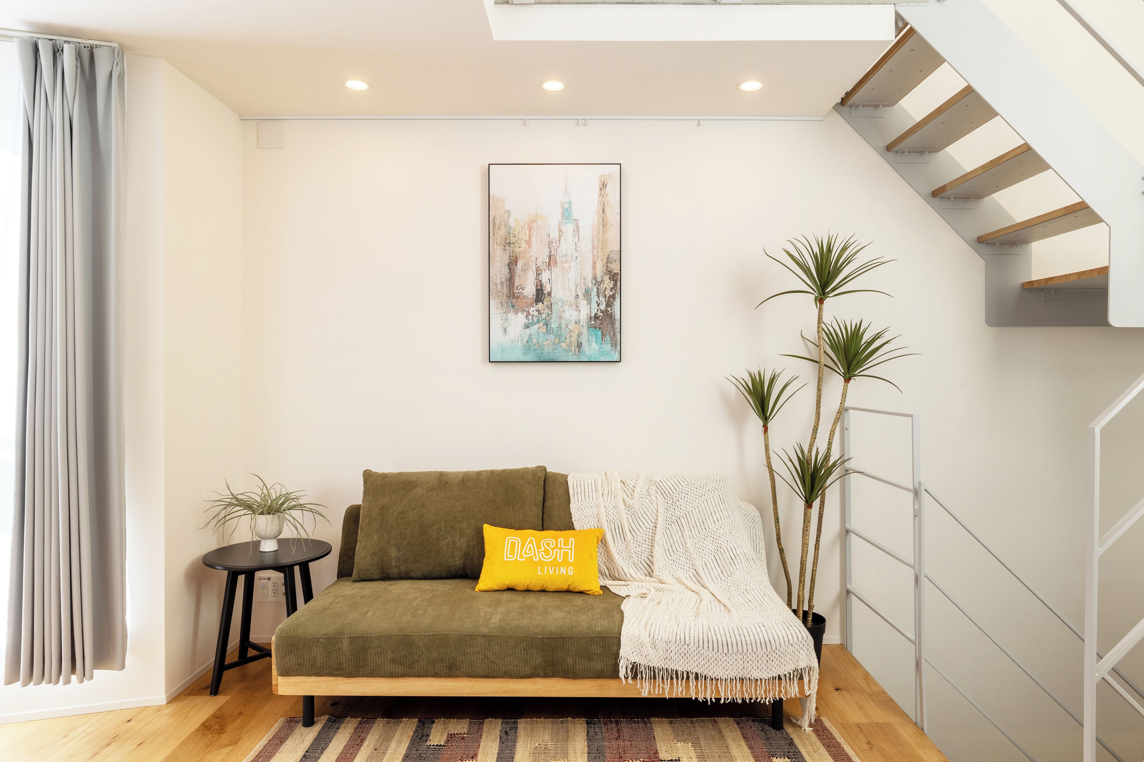 Ein modernes Wohnzimmer mit einer Couch, einem kleinen Tisch, einer Pflanze und einer Treppe.