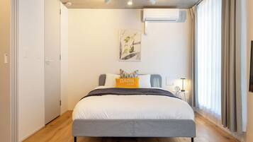 Un dormitorio moderno con cama, mesita de noche y aire acondicionado de pared.