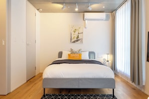 A modern bedroom with a bed, bedside table, and a wall-mounted air conditioning unit. - Dash Living Kagurazaka (Shinjuku City)