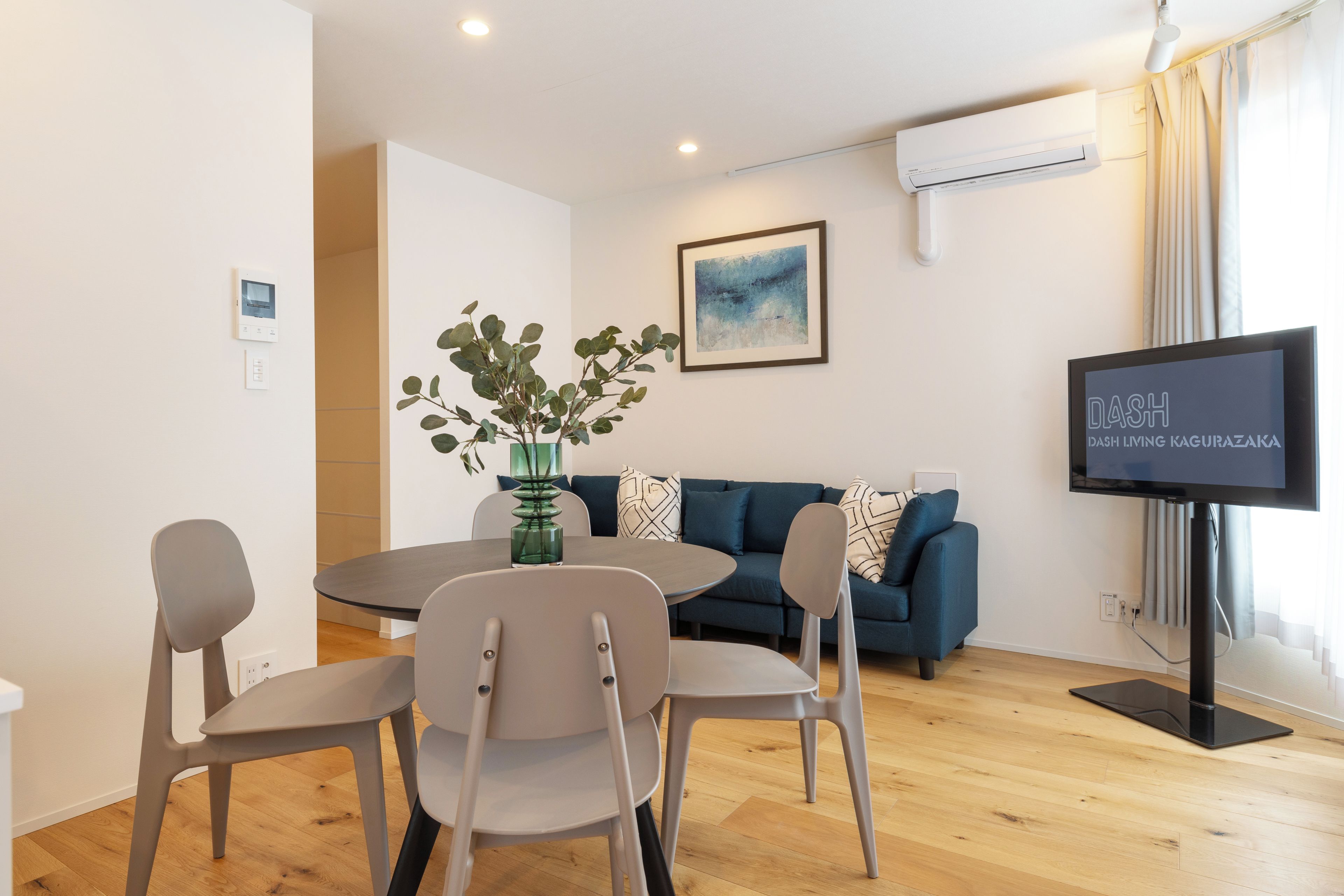 Una sala moderna con una mesa redonda de comedor, dos sillas, un sofá, un televisor y un aire acondicionado instalado en la pared.