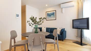 Una sala moderna con una mesa redonda de comedor, dos sillas, un sofá, un televisor y un aire acondicionado instalado en la pared.
