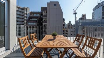 Uma varanda com mesa e cadeiras de madeira, um vaso de planta e vista para edifícios ao redor.