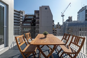 Uma varanda com mesa e cadeiras de madeira, um vaso de planta e vista para edifícios ao redor.