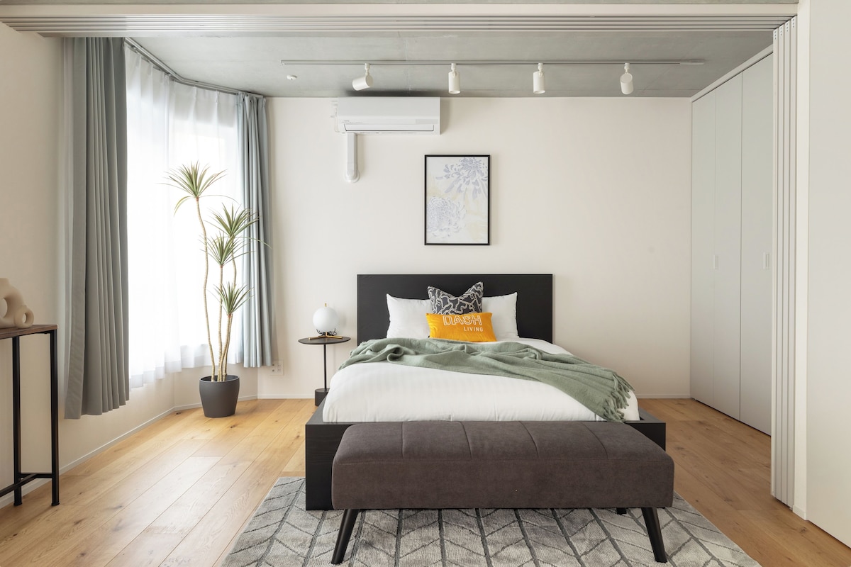 Quarto moderno com cama, mesa de cabeceira, planta em vaso e obra de arte.