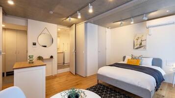 Quarto moderno com cama, mesa de cabeceira e pequeno espaço de trabalho.