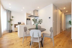 Cozinha moderna com ilha central, área de jantar com mesa redonda e cadeiras, e corredor que leva a uma porta.
