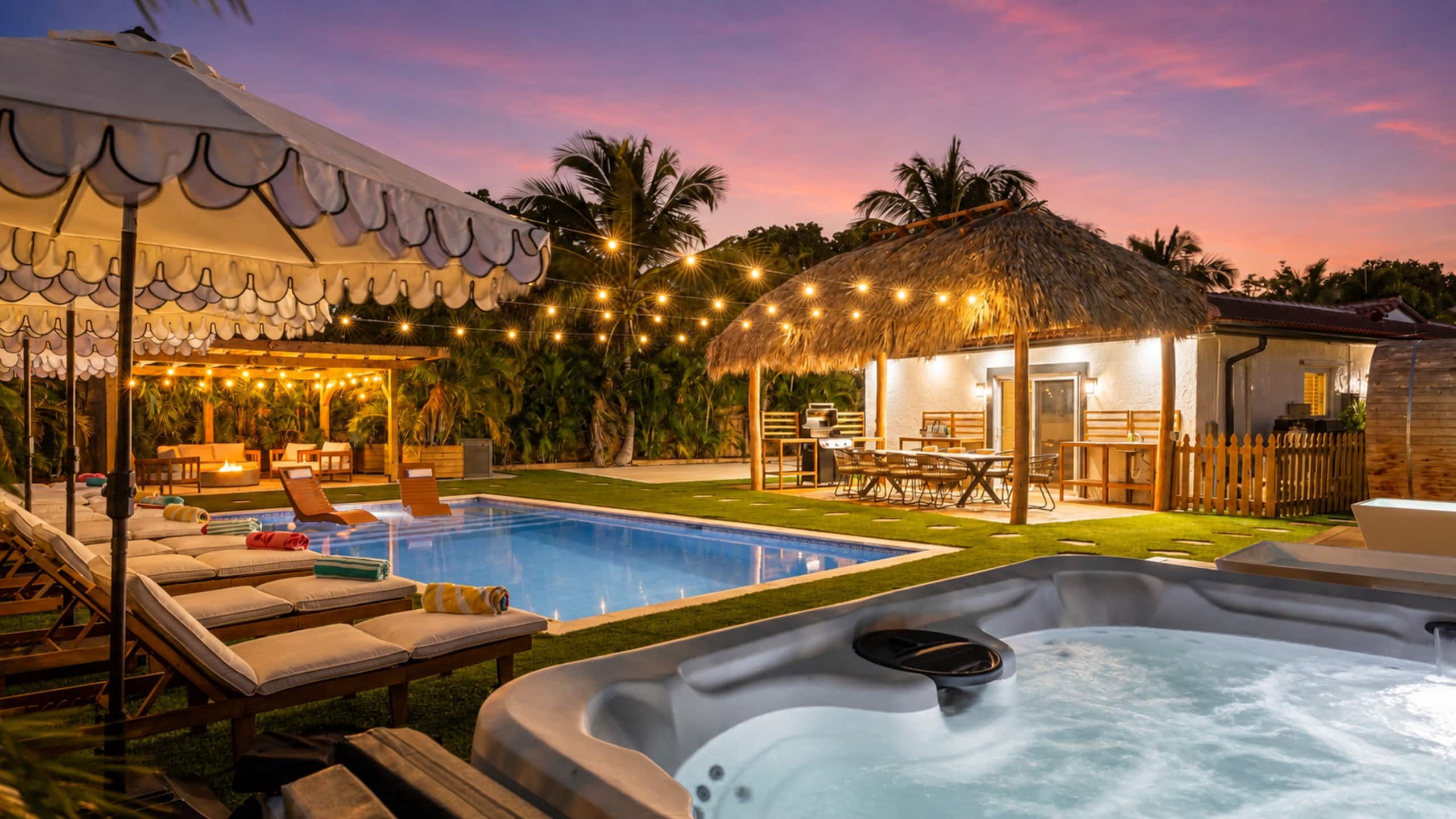 A backyard with a swimming pool, hot tub, lounge chairs, and a covered seating area.