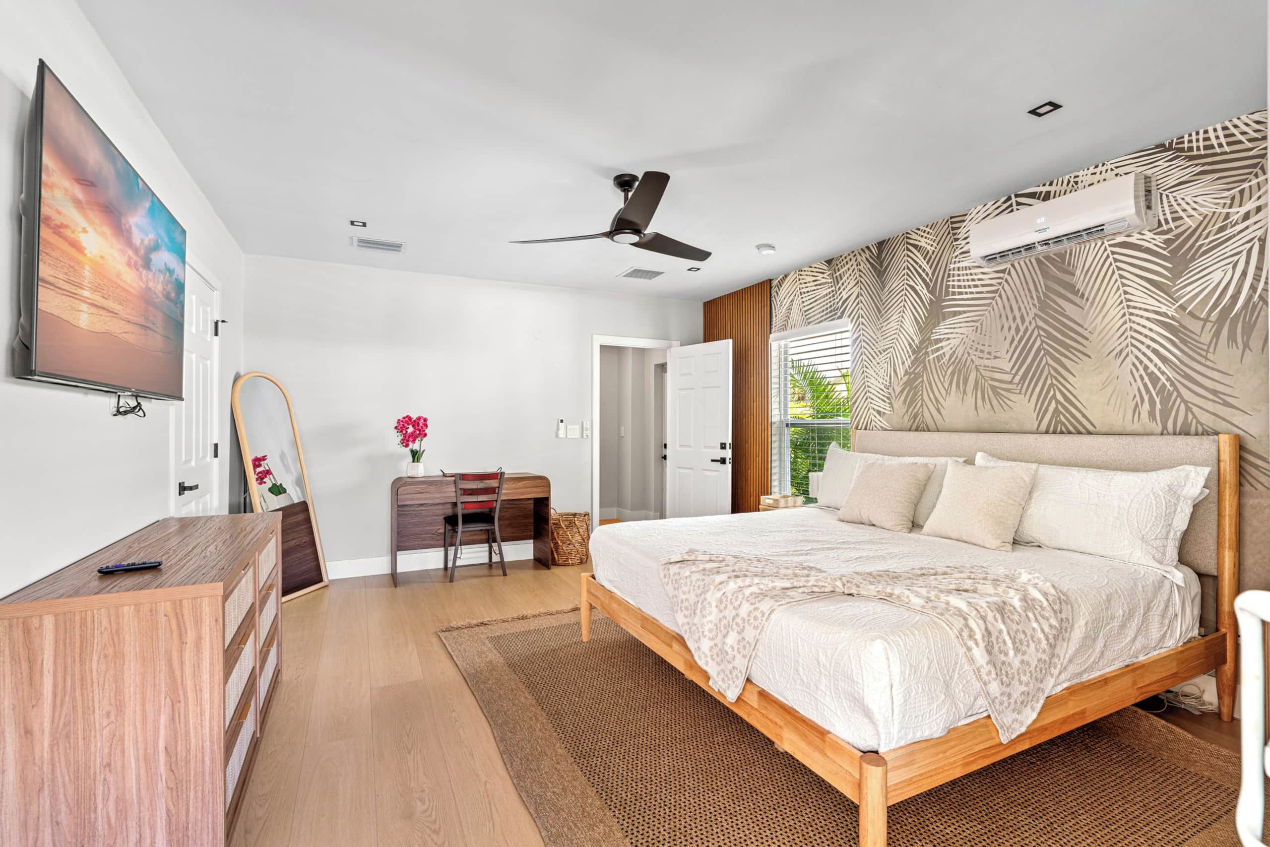 A modern bedroom with a large bed, a desk, and a ceiling fan.