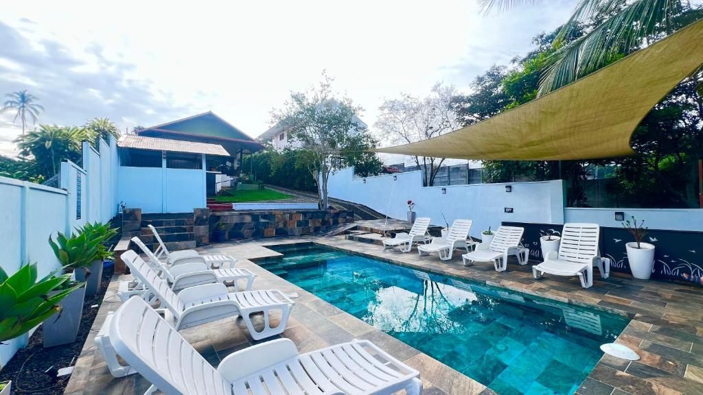 Una piscina con sillas de descanso, una zona sombreada y un edificio blanco al fondo.