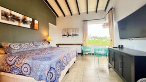 A bedroom with a bed, a desk, a chair, a television, and a window with a view.