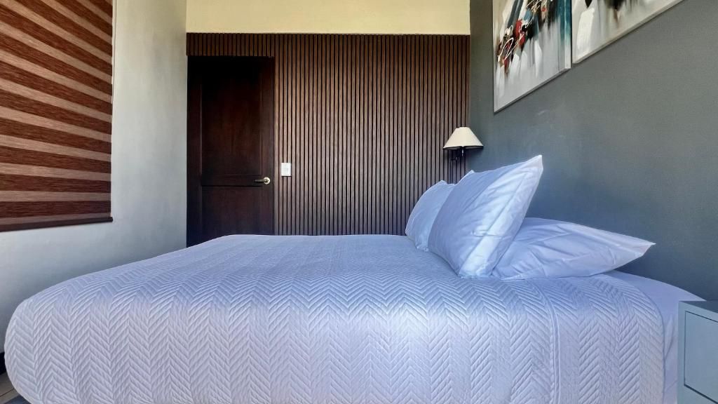 A bedroom with a large bed, a door, a wall-mounted lamp, and a window with blinds.