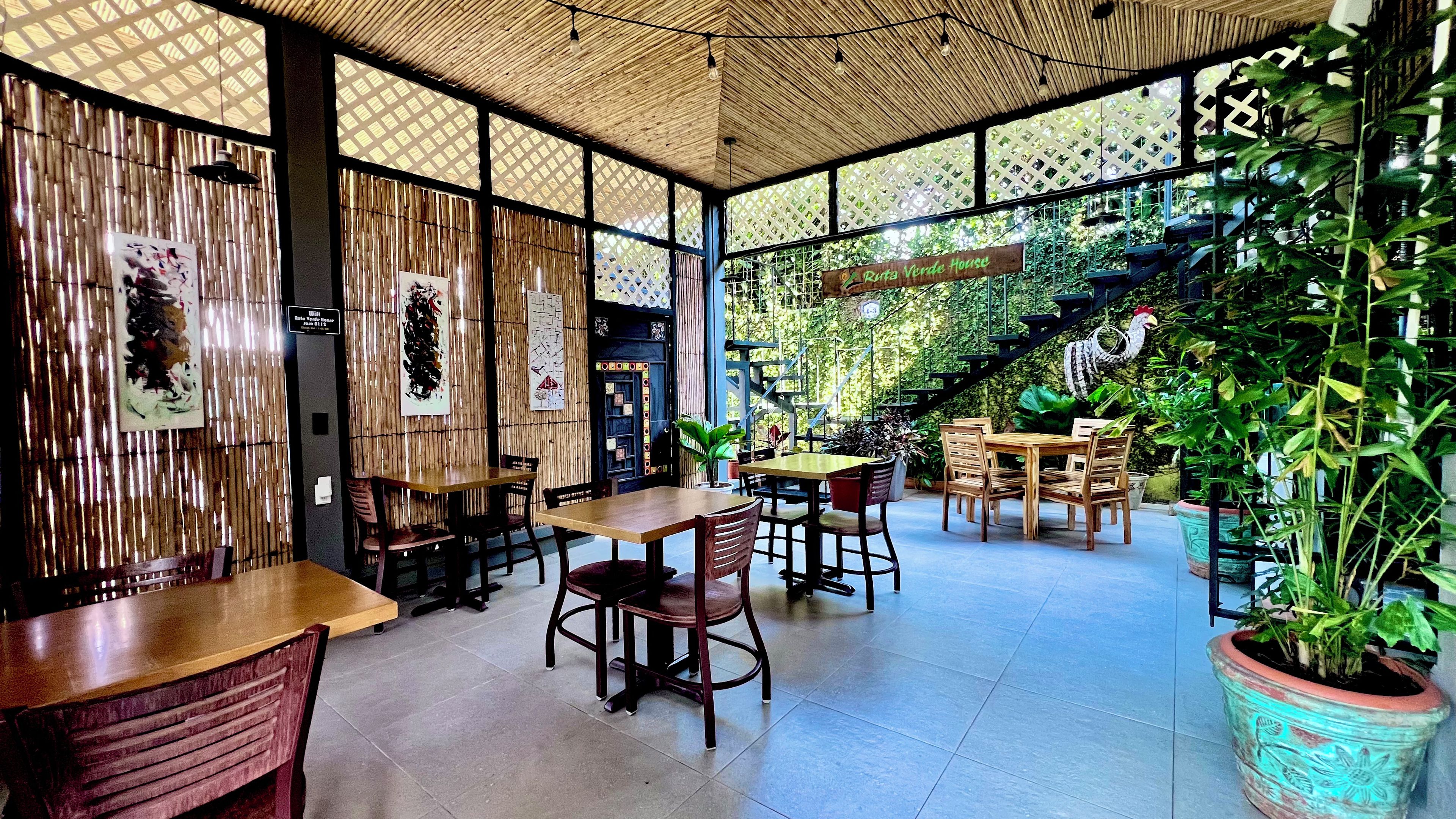 Een restaurant met bamboe wanden, houten tafels en stoelen, en een trap naar een tuingedeelte.