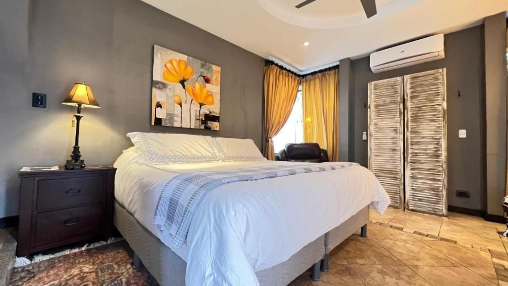 Un dormitorio con cama, mesita de noche, lámpara y un cuadro en la pared.