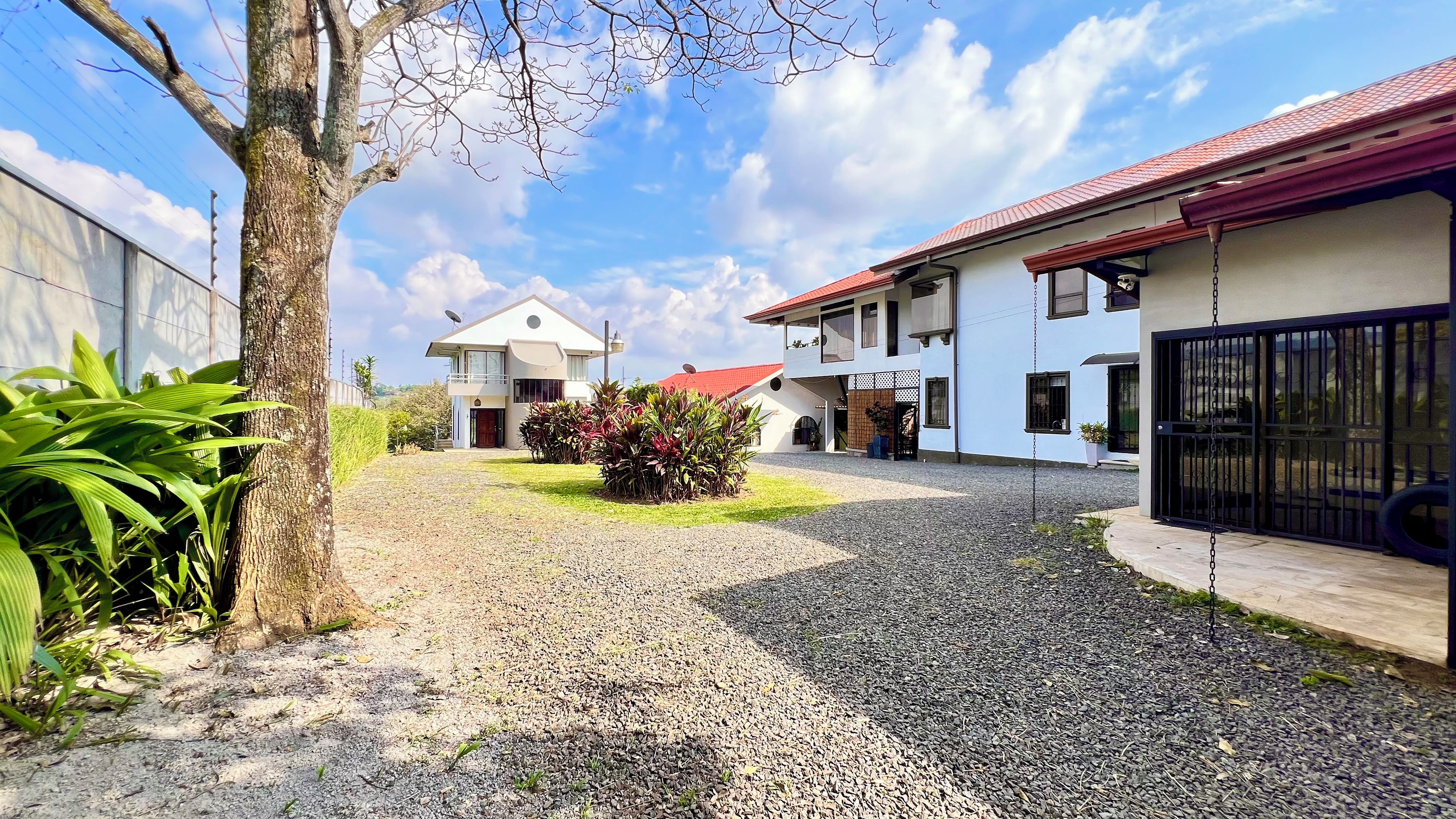 A residential area with a gravel driveway, a house with a red roof, and a tree.