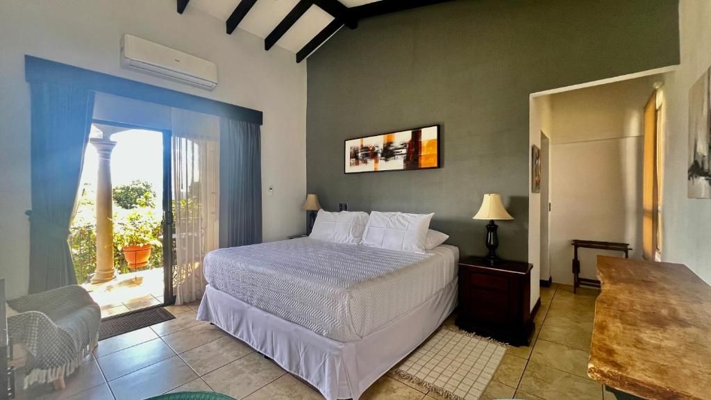 A bedroom with a bed, a nightstand, a lamp, a chair, and a view of the outdoors.