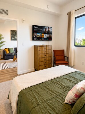 A bedroom with a bed, a wooden dresser, a chair, a TV mounted on the wall, and a window with a view. - Close to Beach | Stylish 1BR + Pullout Sofa (Hollywood)