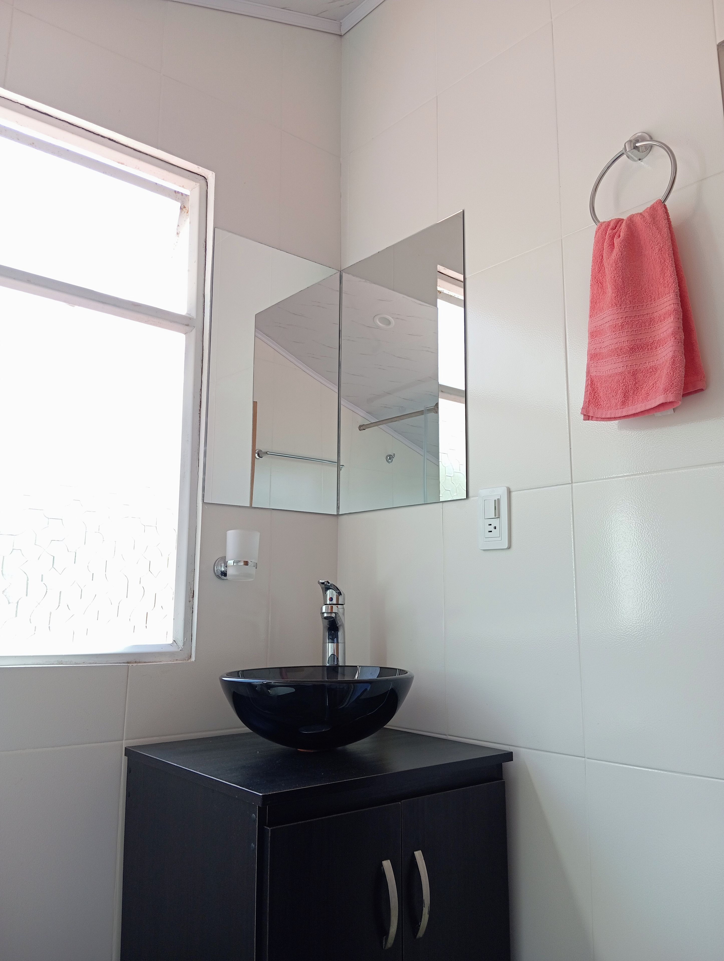 A bathroom with a black cabinet, a glass sink, a mirror, and a window.