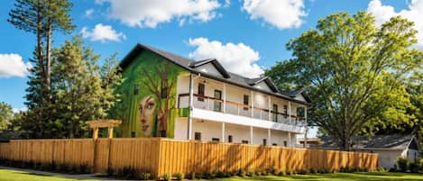 A two-story building with a green mural on the side, a wooden fence, and a well-maintained lawn.