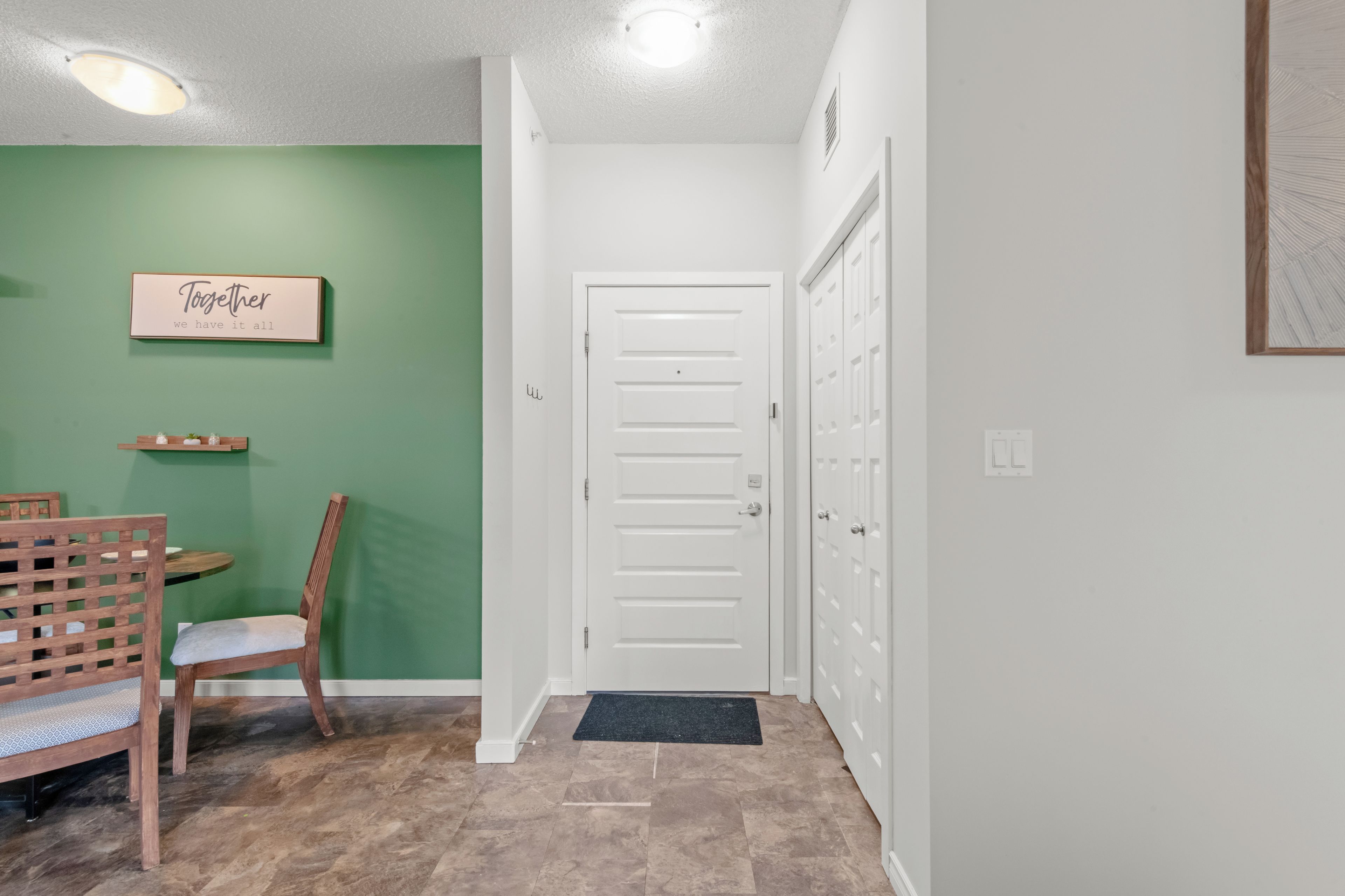 A hallway with a green wall, a white door, a wooden chair, and a small table with a sign above it.