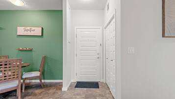 A hallway with a green wall, a white door, a wooden chair, and a small table with a sign above it.