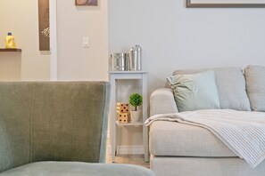 Un salon avec un canapé gris, une petite table d’appoint blanche agrémentée d’objets décoratifs et un fauteuil gris.