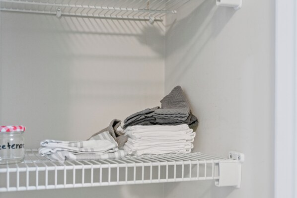 Une étagère blanche avec des serviettes pliées et un bocal dans un espace de rangement.