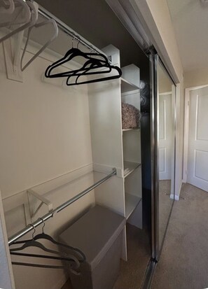Un vestidor con estantes abiertos, una barra para colgar ropa y una puerta que da a otra habitación.