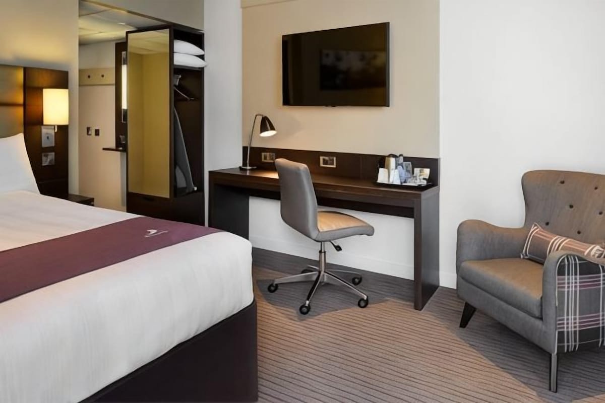 A hotel room with a bed, desk, chair, and a television.