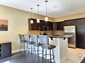 A modern kitchen with dark wood cabinets, stainless steel appliances, and a bar area with stools. - Mountain View Home / Pet Friendly / AC (Invermere)