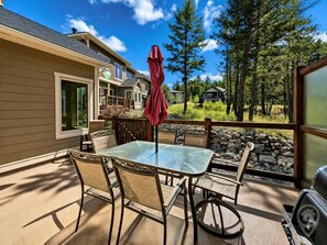 A patio with a glass table and chairs, a red umbrella, and a stone wall. - Mountain View Home / Pet Friendly / AC (Invermere)