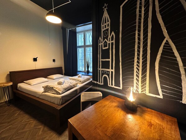 Un dormitorio con cama, una mesa de madera, un mural en la pared y una ventana.