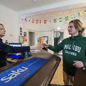 Una persona con sudadera verde con el texto 'Malibu California', parada frente a un mostrador con una alfombra azul que dice 'Saku' y 'KIRU 1870'.