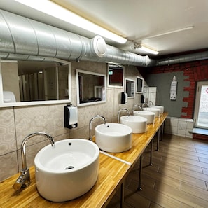 Baño público con varios lavamanos, espejos y secamanos.