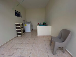 A small, tiled room with a washing machine, a chair, and a sink.
