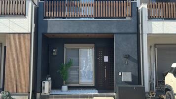 A modern two-story residential building with a dark facade, a balcony with wooden railings, and a garage door.