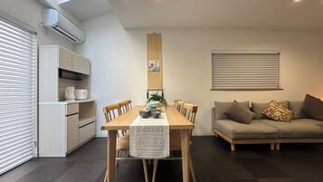 A modern living space with a dining table, chairs, a sofa, and a kitchen area.